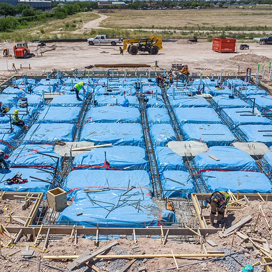 A construction site for commercial purposes, with blue tarps draped over various structures and equipment.